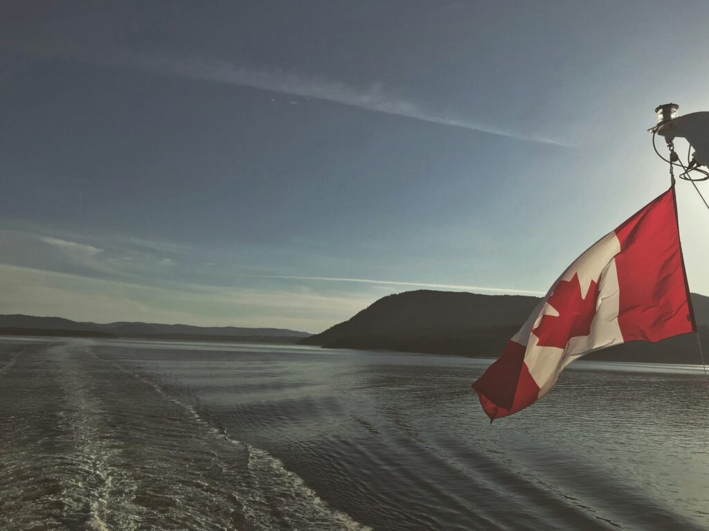 image of a canadian flag waving in the wind off the back of a boat on a lake in canada